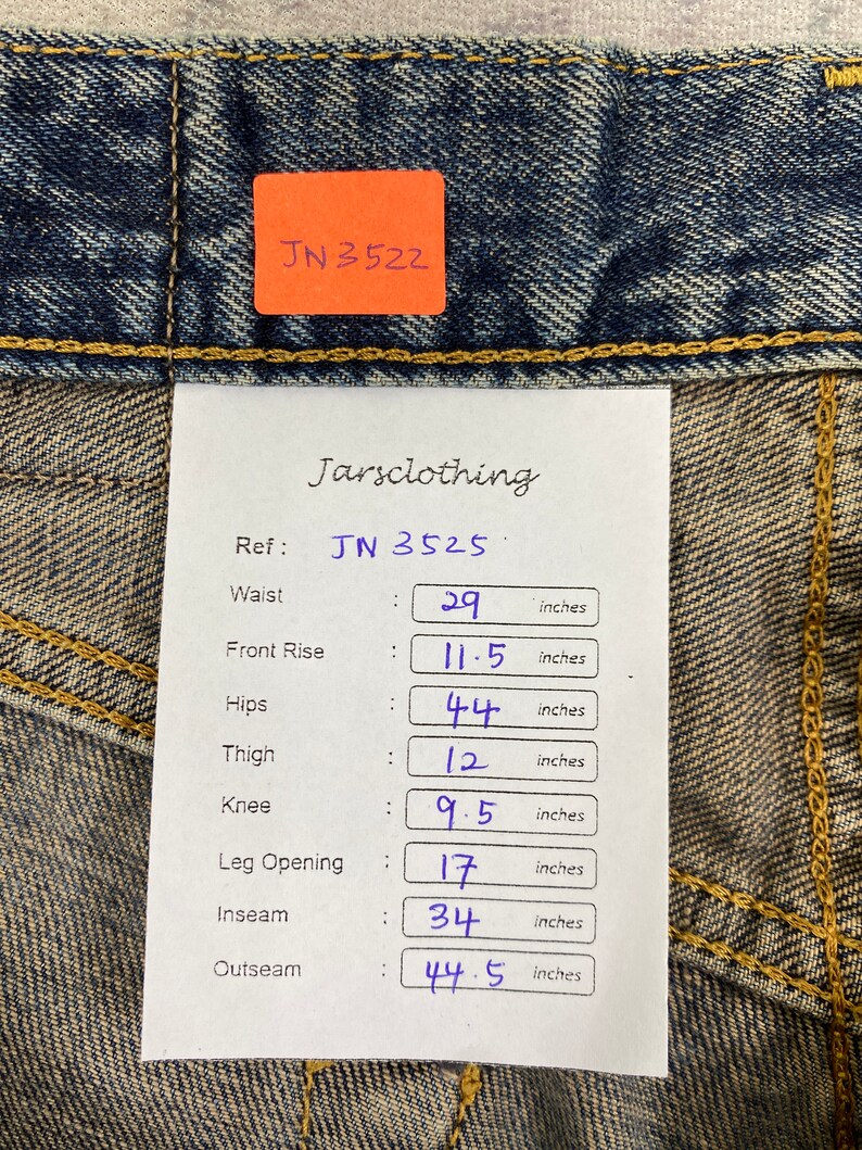 May include: Close-up of blue denim jeans with a tag displaying measurements. Waist is 29 inches, front rise 11.5 inches, hips 44 inches, thigh 12 inches, knee 9.5 inches, leg opening 17 inches, inseam 34 inches, and outseam 44.5 inches.