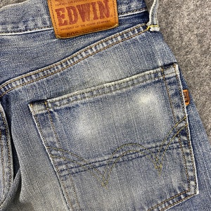 May include: Close-up of light blue denim jeans with a faded wash. The back pocket is visible, along with the Edwin brand leather patch. The patch reads "EDWIN" and "505".