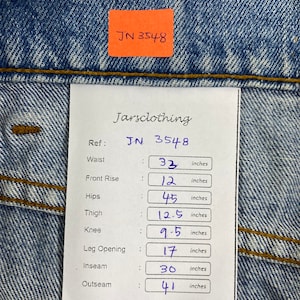 K&ouml;nnte beinhalten: Nahaufnahme einer blauen Jeans mit einem Etikett mit der Aufschrift "JN 3548". Die Taille misst 83,8 cm, die vordere Leibh&ouml;he 30,5 cm, die H&uuml;fte 114,3 cm, der Oberschenkel 31,8 cm, das Knie 24,1 cm, die Bein&ouml;ffnung 43,2 cm, die Innenbeinl&auml;nge 76,2 cm und die Au&szlig;enbeinl&auml;nge 104,1 cm.