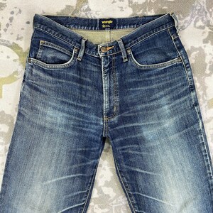 May include: A pair of blue denim jeans with a faded look. The jeans have a classic five-pocket style and a Wrangler brand label on the back waistband.
