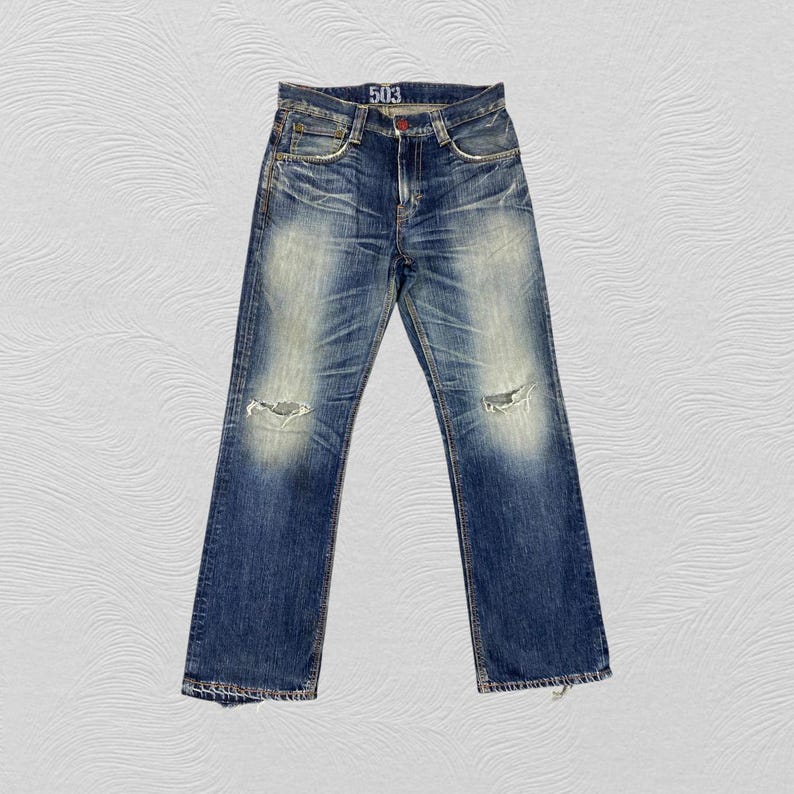 May include: Blue denim jeans featuring a distressed wash with faded areas on the thighs and knees. The jeans include a button fly, five pockets, and small rips on both knees. The interior waistband label displays the number 503 in white text.
