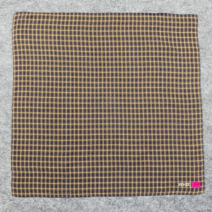 May include: A square, folded fabric with a grid pattern of yellow lines on a dark navy blue background. The lower right corner features a pink tag with the word "KENZO" in white text.