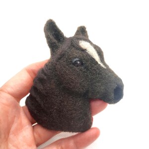 以下が含まれることがあります： 茶色の体と顔に白いストライプのある、手作りのフェルト製の馬の頭部の彫刻。彫刻は羊毛で作られており、リアルな外観をしています。
