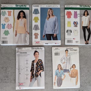 May include: Five sewing pattern envelopes from Simplicity and Very Easy Vogue. The patterns feature images of women wearing the finished garments. The patterns include tops, blouses, and jackets. The envelopes are various colors, including blue, pink, and white.