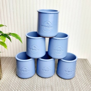 May include: Six pale blue ceramic pots stacked in a pyramid. Each pot features a rounded rim and the embossed word "FERMIERE". The pots are arranged on a light-coloured surface.