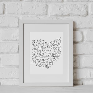 May include: A white framed print with black calligraphy that says "Ohio" multiple times in a heart shape.