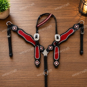 May include: A black leather horse breast collar featuring red suede inlays, silver-toned metal buckles, and decorative square conchos with red and white crystal accents. The harness includes adjustable straps with metal hardware and a central connector.