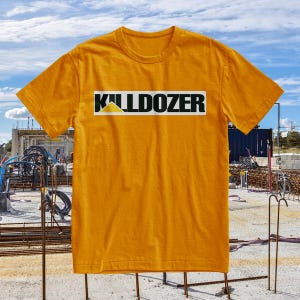 Może przedstawiać: Musztardowa koszulka z napisem "KILLDOZER" czarnymi literami w białym prostokącie. Żółty trójkąt znajduje się nad literą "L" w słowie "KILLDOZER". Koszulka jest krótka i wykonana z miękkiego materiału.