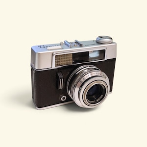 Op de afbeelding: Een vintage Vitoret LR 35mm filmcamera met een zwarte, getextureerde behuizing en een zilveren bovenplaat. De camera is voorzien van een Color-Lanthar lens, een zoeker, een ontspanknop en een flitsschoen op de bovenzijde.