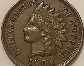May include: A copper-colored 1906 Indian Head penny. The coin features a profile of a Native American in a feathered headdress, with the words "LIBERTY" and "UNITED STATES OF AMERICA" inscribed around the edges.