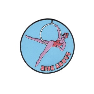 May include: A blue and white embroidered patch featuring a woman in a red leotard hanging from a hoop. The text "Rise Above" is embroidered in white on the patch.