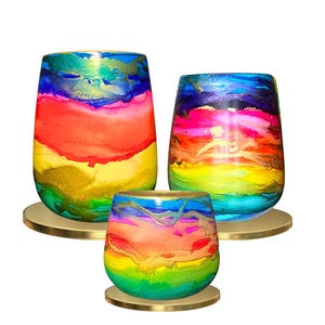 May include: Three glass candle holders with a rainbow design. The candle holders are different sizes and are sitting on gold metal bases.