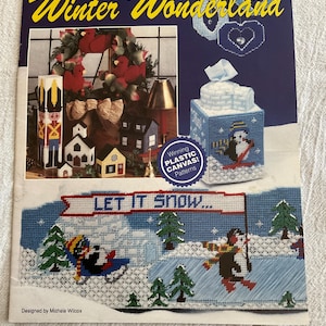May include: A craft pattern book titled "Winter Wonderland" featuring needlecraft designs. The cover displays a variety of winter-themed plastic canvas projects, including a tissue box cover with a penguin, and a scene with the text "LET IT SNOW...".