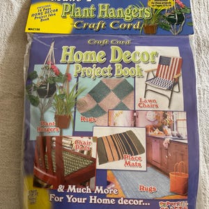 May include: A craft kit for making home decor items. The package includes instructions for plant hangers, rugs, chair pads, and place mats. The kit features the text "Make 2 Plant Hangers Craft Cord Home Decor Project Book".