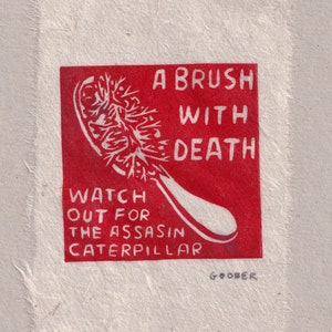 Könnte beinhalten: Roter rechteckiger Druck mit einem weißen Pinsel und dem Text "A brush with death, watch out for the assassin caterpillar" und der Unterschrift "Goober".