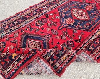 Könnte beinhalten: Ein roter, blauer und cremefarbener Vintage-Teppich mit geometrischem Muster. Der Teppich ist in der Mitte gefaltet und hat einen Fransenrand.