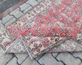 May include: A vintage rug with a floral pattern in shades of pink, cream, and beige. The rug is folded in half, showing the intricate details of the design.