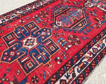 Könnte beinhalten: Ein roter, blauer und weißer Teppich mit geometrischem Muster. Der Teppich hat einen Fransenrand und ist aus Wolle.