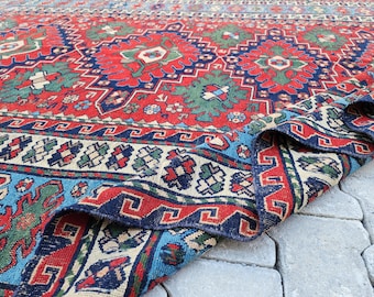 May include: A vintage rug with a red, blue, and green geometric pattern. The rug is folded in half and the edges are visible.