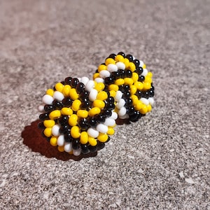 May include: A pair of black, white, and yellow beaded earrings. The beads are arranged in a circular pattern.