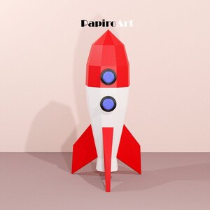 May include: A red, white, and blue rocket ship with a geometric design. The rocket has two blue portholes and red fins. The text "PapiroArt" is at the top of the image.