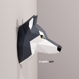 May include: A grey and white papercraft wolf head sculpture mounted on a wall. The wolf's eyes are yellow and the sculpture is made of folded paper. The text "PapirOArt" is visible at the bottom of the image.