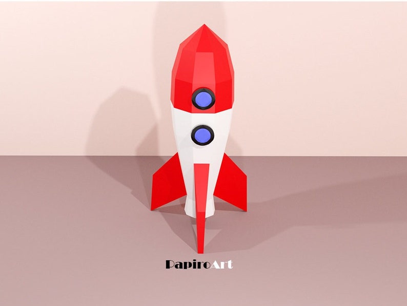 May include: A geometric rocket model in red, white, and blue. The rocket features a pointed top, two circular windows, and red fins. The word "PapiroArt" is printed at the bottom.