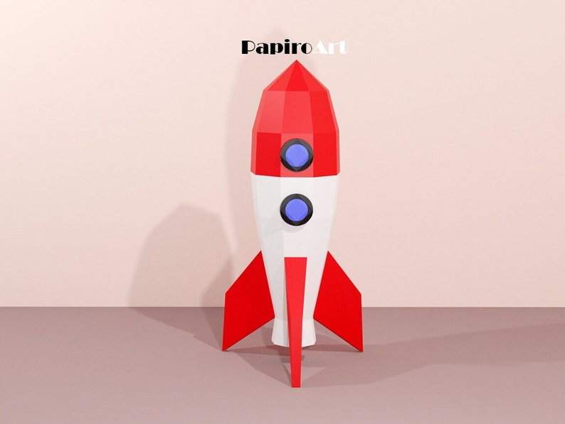 May include: A red, white, and blue rocket ship with a geometric design. The rocket has two blue portholes and red fins. The text "PapiroArt" is at the top of the image.