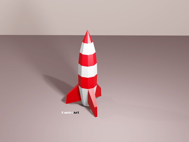 May include: A red and white paper rocket with a pointed nose and fins. The rocket is standing on a light brown surface.