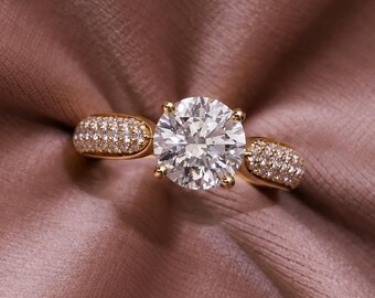 May include: A gold ring featuring a large, round, brilliant-cut center stone held by four prongs. The band is accented with small, pavé-set stones on both sides of the center setting, creating a sparkling, detailed appearance on the metal band.