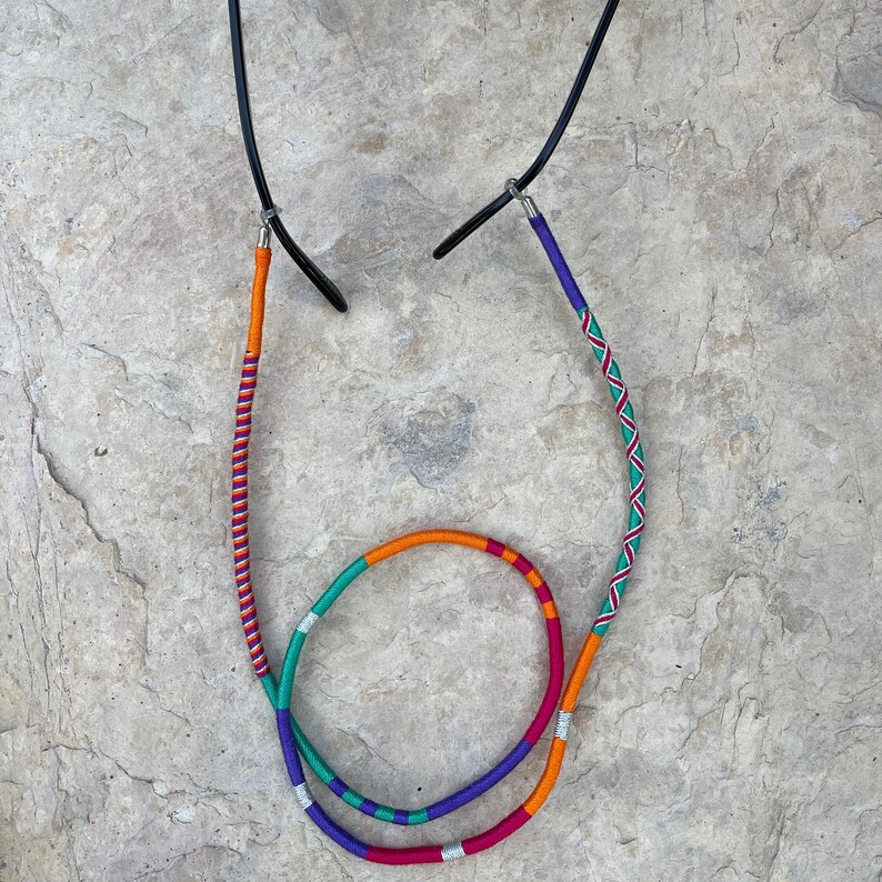 May include: A pair of glasses with a colorful, multi-strand cord. The cord is made of orange, red, purple, green, and silver thread.