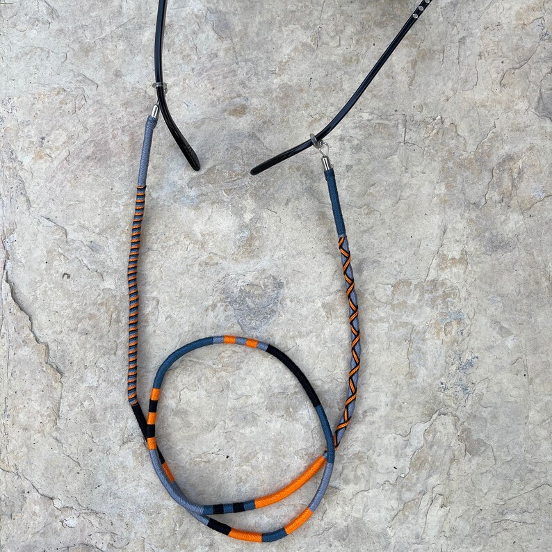 May include: A pair of glasses with a blue and orange braided cord. The cord is attached to the glasses with metal clasps.