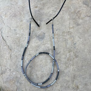 May include: A gray and black glasses chain with silver metal ends. The chain is made of woven cord and is designed to hold glasses around the neck.