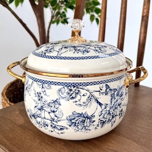 May include: White enamel pot with a blue and white floral pattern and gold accents. The pot has a glass knob on the lid and two gold handles.
