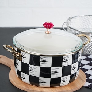 Puede incluir: Olla de esmalte a cuadros en blanco y negro con un pomo rojo en la tapa. La olla está sobre una tabla de cortar de madera.