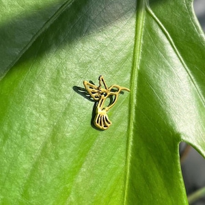 May include: A gold-colored hummingbird cutout, with intricate details, is placed on a green leaf.