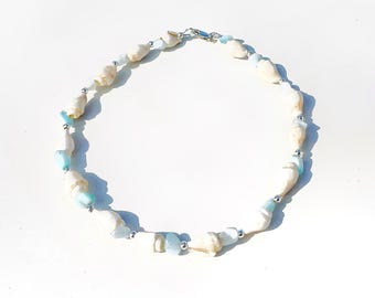 May include: A white and blue seashell necklace with silver beads. The necklace is made of natural materials and has a simple, elegant design.