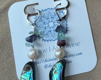 May include: Dangle earrings featuring silver-tone leverback hooks, small tumbled fluorite stones in shades of green and purple, a single white round pearl, and a large, iridescent, dark-toned abalone shell pendant at the base of each earring.