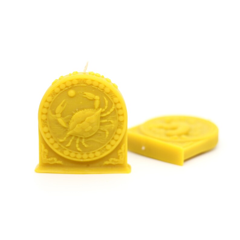 May include: Two yellow beeswax candles, one with a raised design of a crab, the other with a raised design of a fish.