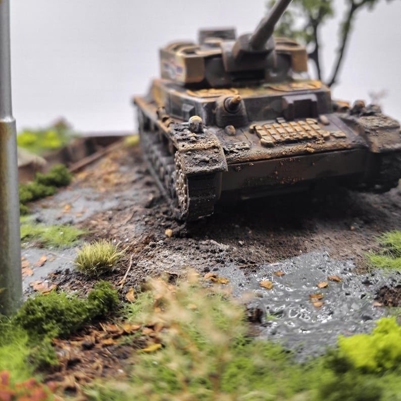 May include: A detailed miniature model of a military tank, showcasing a weathered, battle-worn appearance. The tank is painted in shades of brown and green, with visible rust and dirt. The model sits on a diorama base with grass and muddy terrain.