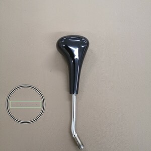 May include: Black plastic gear shift knob with a chrome metal shaft. The knob has a rounded, teardrop shape.