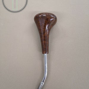 Op de afbeelding: Een bruine houten en chromen versnellingspookknop. De knop heeft een houtnerfpatroon en een chromen steel.