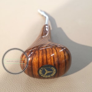 Puede incluir: Una palanca de cambios de madera con el logotipo de Mercedes-Benz. La palanca es de color marrón con un patrón de veta de madera y tiene una palanca de metal plateado.