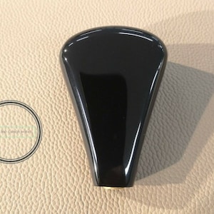 Könnte beinhalten: Schwarzer Schaltknauf mit glatter, glänzender Oberfläche. Der Knauf hat eine abgerundete, tropfenförmige Form und eine goldene Metallbasis.