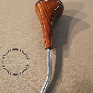 Puede incluir: Una perilla de cambio de marchas de madera con un acabado de grano de madera marrón y un eje de metal cromado.