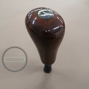 Può includere: Un pomello del cambio in legno marrone con un logo Mercedes-Benz dorato.