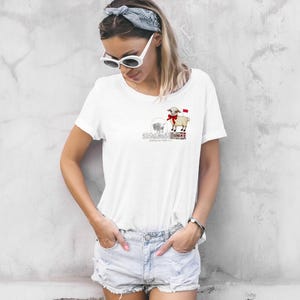 May include: White t-shirt with a graphic of a sheep wearing a red bow and standing on a box. The text "Shepherds of the City" is printed below the sheep.