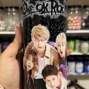 May include: A black and white tumbler with a graphic of the band "ONE OK ROCK" and four band members. The tumbler has a white lid.