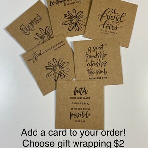 以下が含まれることがあります： インスピレーションを与える引用と花のイラストが描かれた、茶色のクラフト紙製のカード10枚セット。カードには、「強く、勇敢であれ」、「友人はいつも愛してくれる」、「神と共に、すべては可能である」、「甘い友情は心をリフレッシュする」、「信仰は物事を簡単にはしない、可能にする」などの引用が書かれている。