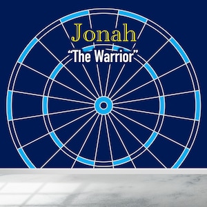Puede incluir: Un tablero de dardos azul y blanco con el nombre "Jonah" y el texto "The Warrior" en letras amarillas.